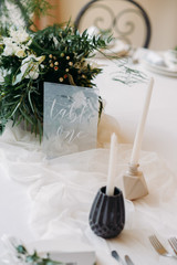 Decorated tables with plates, knives, forks and bouquet with white flowers and greens on the centre