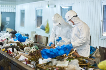 Portrait of two workers  wearing biohazard suits and hardhats working at waste processing plant...