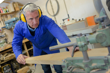 Naklejka na ściany i meble senior carpenter using bandsaw to cut wooden plank in workshop