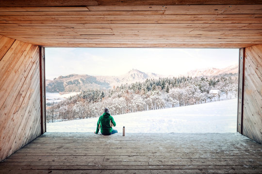 Man sits in wooden hangar wit view on snowy  mountain valley