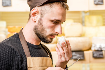 Portrait of a handsome cheese seller in uniform smelling young cheese in front of the store showcase