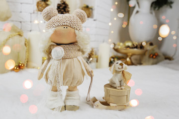 Christmas toy doll with wooden sleigh on which sits a toy dog on a background of Christmas lights.