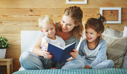 family mother reading to  children book in bed.