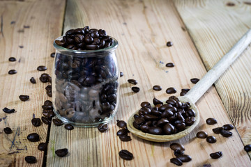 Fototapeta na wymiar Coffee beans in jar and wooden spoon, wooden table