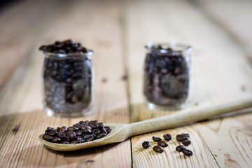 Fototapeta na wymiar Coffee beans in jar and wooden spoon, wooden table