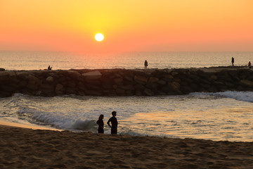 Amazing sunset over a beach with a jetty. With a couple watching the sea.