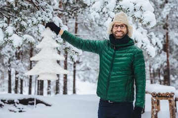 Happy delightful middle aged male with beard and mustache, wears warm jacket and hat, holds...