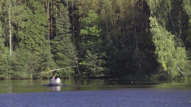 Two fisherman in rubber boat floats rowing with oars on river. Man is fishing on lake in sunny forest. Stracha river - beautiful place close to Belarusian nuclear power plant