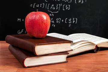 Red apple on books and school blackboard with mathematical equations in the classroom