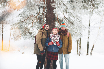 Happy and joyful friends in warm and cozy clothes walk through the winter forest. Сompany of guys and girls are having fun together in a snowy landscape