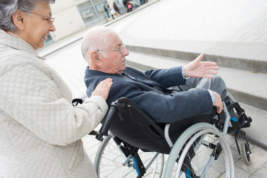 depressed senior man in wheelchair being pushed by wife