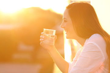 Happy lady holding a glass of water at sunset