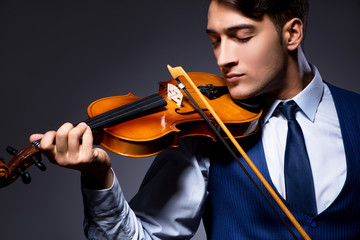 Young man playing violin in dark room