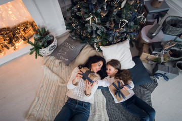 Merry Christmas and Happy Holidays. Cheerful mom and her cute daughter girl exchanging gifts. Parent and little child having fun near Christmas tree indoors. Loving family with presents in room.