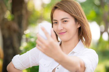 Asian woman holding smartphone digital camera with her hands and taking a selfie