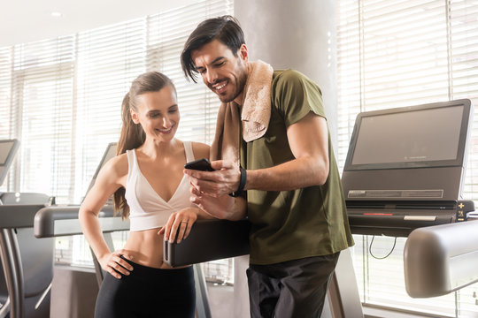 Young couple smiling while communicating on the mobile phone during break at the fitness club
