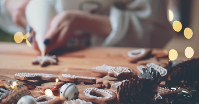 Woman Decorating Baked Gingerbread Christmas Cookies. 4K SLOW MOTION.  Female hands frosting and icing fresh holiday bakery. Festive food, family, Christmas and New Year traditions concept.