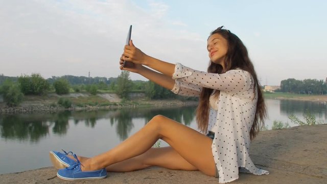 Beautiful girl is photographed in nature. A teenager girl with a tablet takes pictures of herself.