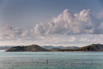 Barrier Reef, Australia - December 3, 2009: brown islands stick out of a azure blue water under a white and gray prominent cloudscape in light blue sky in the Coral Sea.