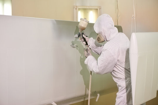 Spray painting, airplane wing. Worker in coverall using airbrush.
