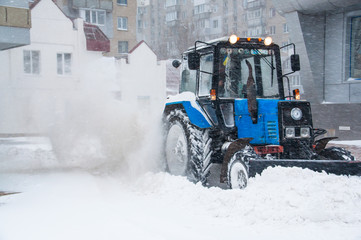 A blue tractor clears snow on the road