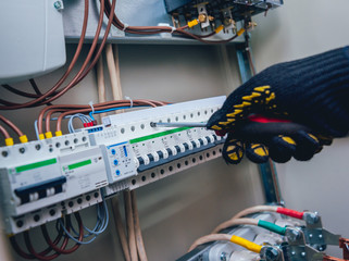 Electricians hands testing switches in electric box. Electrical panel with fuses and contactors