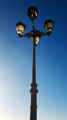 Fototapeta na wymiar Four glass lights on a single ornamental metal pole set against a deep clear blue sky