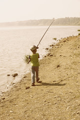 little boy walks with a fishing rod along the shore to fish early morning