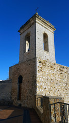 Fototapeta na wymiar Old stone belltower with wooden door and metal cross. Blue clear sky.