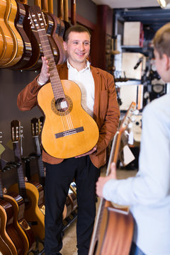 Adult male seller showing guitar to boy client