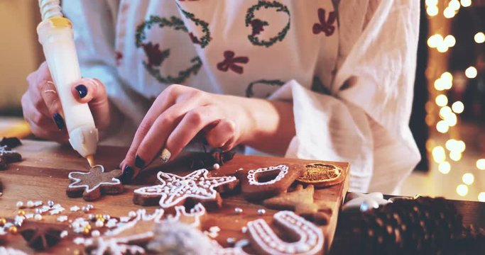 Woman Decorating Baked Gingerbread Christmas Cookies. 4K SLOW MOTION.  Female hands frosting and icing fresh holiday bakery. Festive food, family, Christmas and New Year traditions concept.