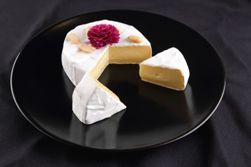 Cheese, camembert on a black plate, honey, pink flower, sliced cheese with mildew on a black velvet, minimalism, cheese on a black background
