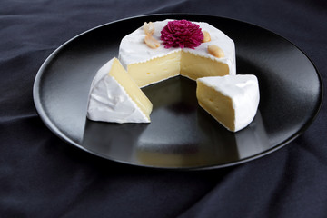 Cheese, camembert on a black plate, honey, pink flower, sliced cheese with mildew on a black velvet, minimalism, cheese on a black background