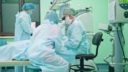 Obraz premium Team of ophtalmology surgeons and assistants with ophtalomological surgery tools during surgical treatment. Female and male surgeons operate the machinery. Indoor. Medium.