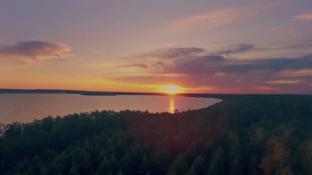 AERIAL: Beautiful view of huge lake during colorful sunset. Amazing nature landscape with green forest and blue water.