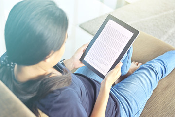 Woman relaxing at home reading an e-book online on her tablet