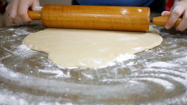 Woman rolls some dough with wooden roller