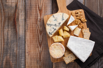 Tasting cheese dish on a wooden plate. Food for wine and romantic, cheese delicatessen on a wooden rustic table. Top view with copy space