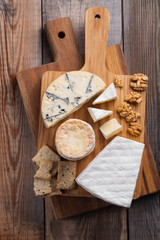 Tasting cheese dish on a wooden plate. Food for wine and romantic, cheese delicatessen on a wooden rustic table. Top view