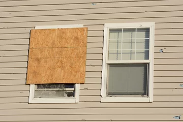 Blackout roller blinds Storm Boarded up window and hail storm damage on house siding and window frame
