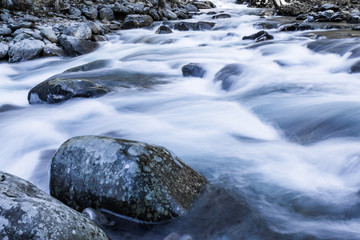 Swiftly moving river water over and around large rocks winter landscape, horizontal aspect