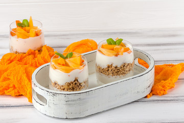 Persimmon creamy trifle in beautiful glasses, fresh ripe fruit slices on white wooden background. Healthy vegetarian food. Delicious dessert. Close up photography. Selective focus.