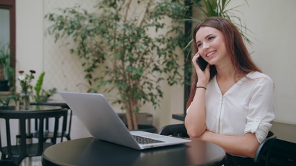 A beautiful girl speaking on the mobile phone in front of an open laptop in the room. Glitch. Medium shot. Soft focus.