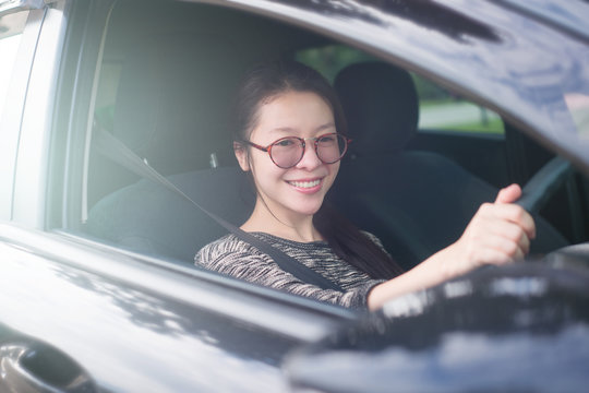 Attractive cute young asian woman in casual wear looking forward while driving a car. smile and happy time to travel or rest concept. filtered image. soft light effect added. fasten seat belt.