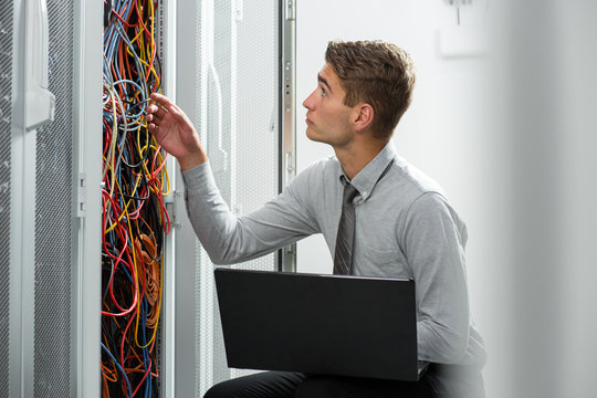 Portrait of modern young man holding laptop standing in server room working with supercomputer