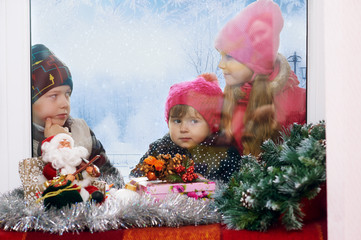 Children standing outside the window on a winter day looking out the window at the winter gifts . Merry Christmas