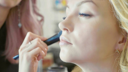 Young makeup artist applying concealer on model's face.