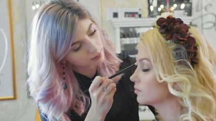 Young makeup artist applying cosmetics on model's eyes.