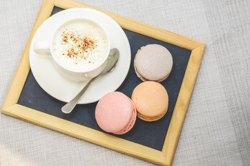 Cake macaroon on the plate,cinnamon and a frothy coffee close up