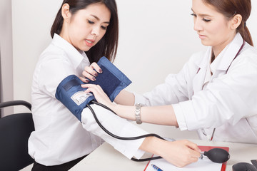 Doctor using sphygmomanometer with stethoscope checking blood pressure  to a patient in the...